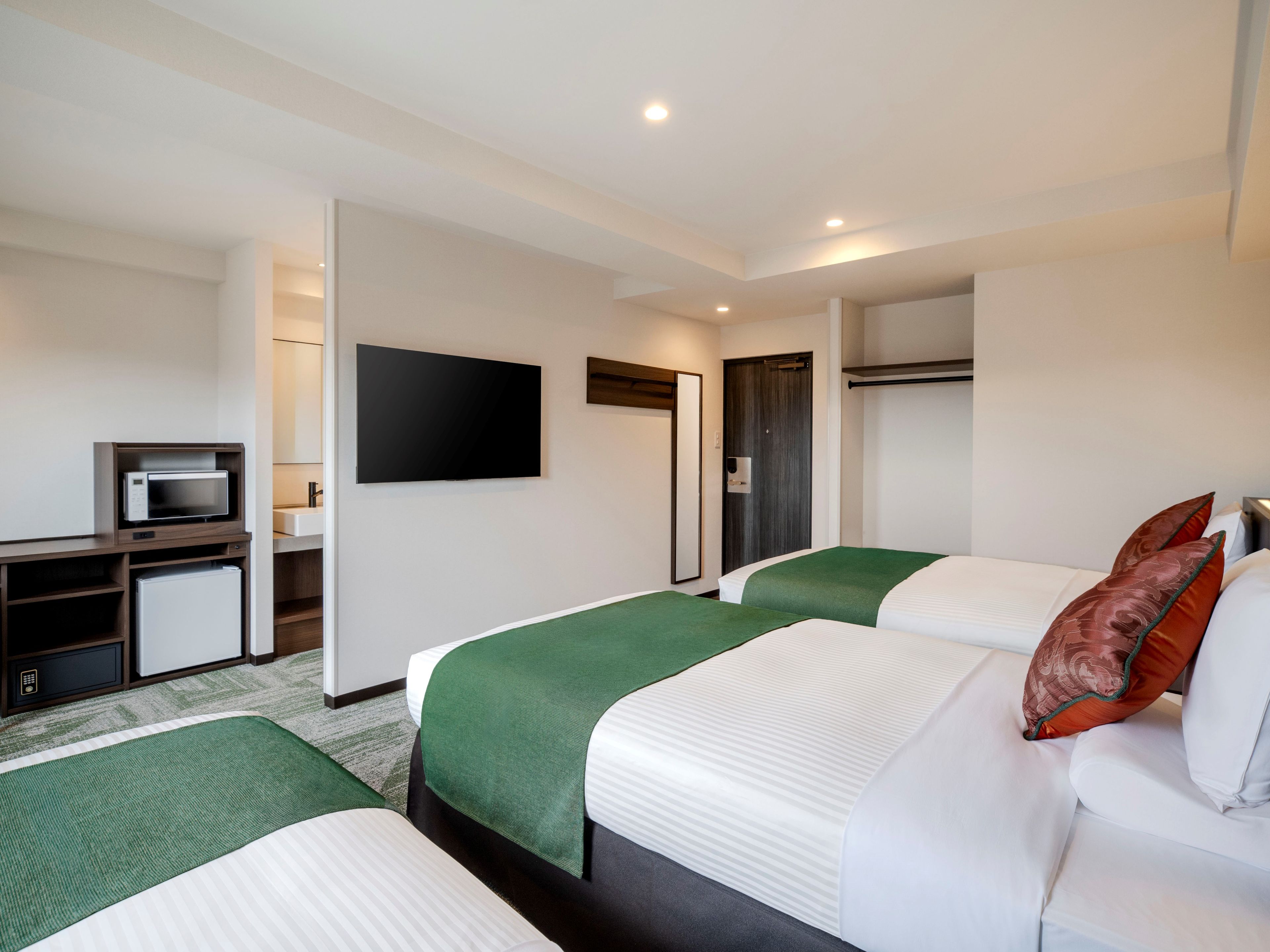 Une chambre d’hôtel avec deux lits, une télévision, un bureau avec un micro-ondes et une porte.