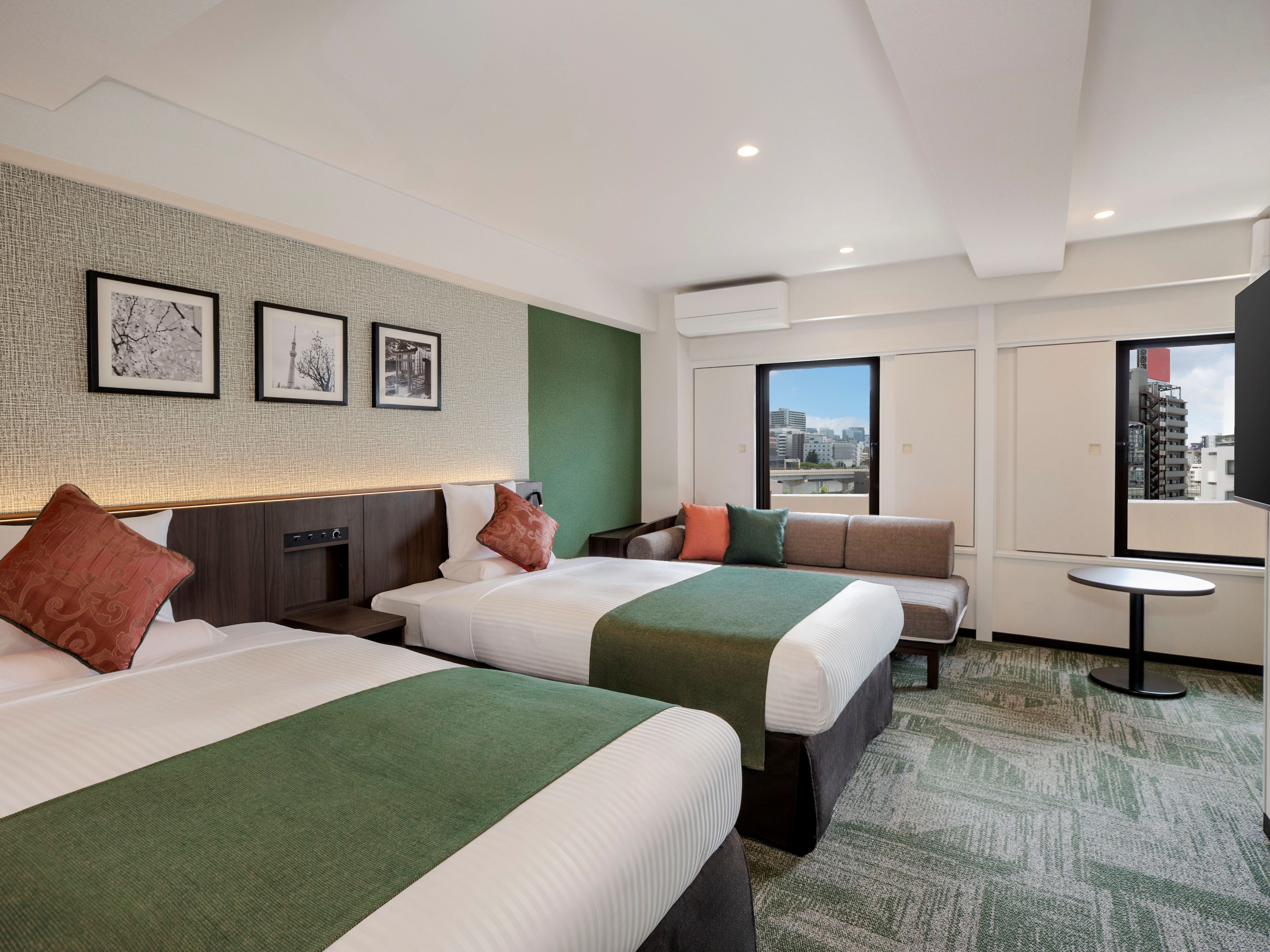 A hotel room with two beds, a sofa, a small table, and a city view.