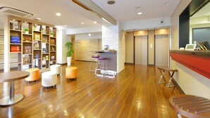 A modern hotel lobby with wooden flooring, a reception desk, a bar area, and a seating area with round tables and ottomans. - Hotel MyStays Asakusa (Tokyo)