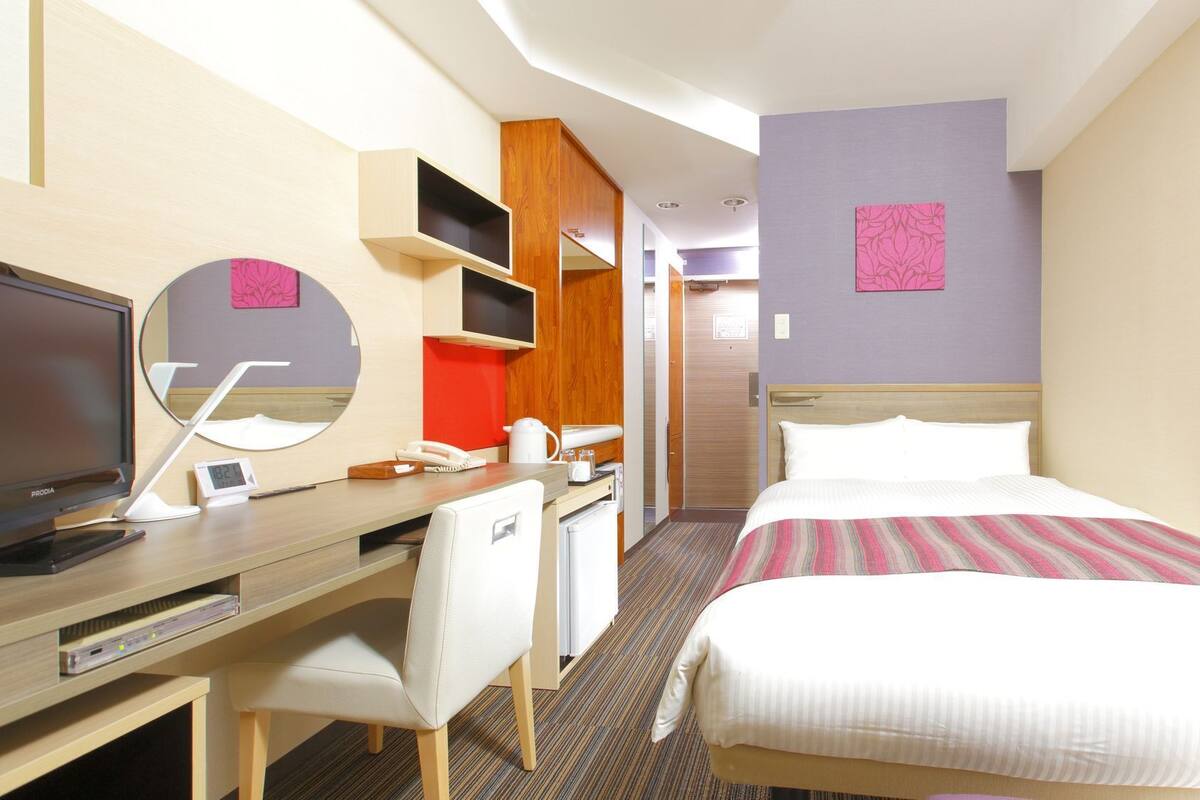 A hotel room with a bed, desk, chair, TV, and a mirror.