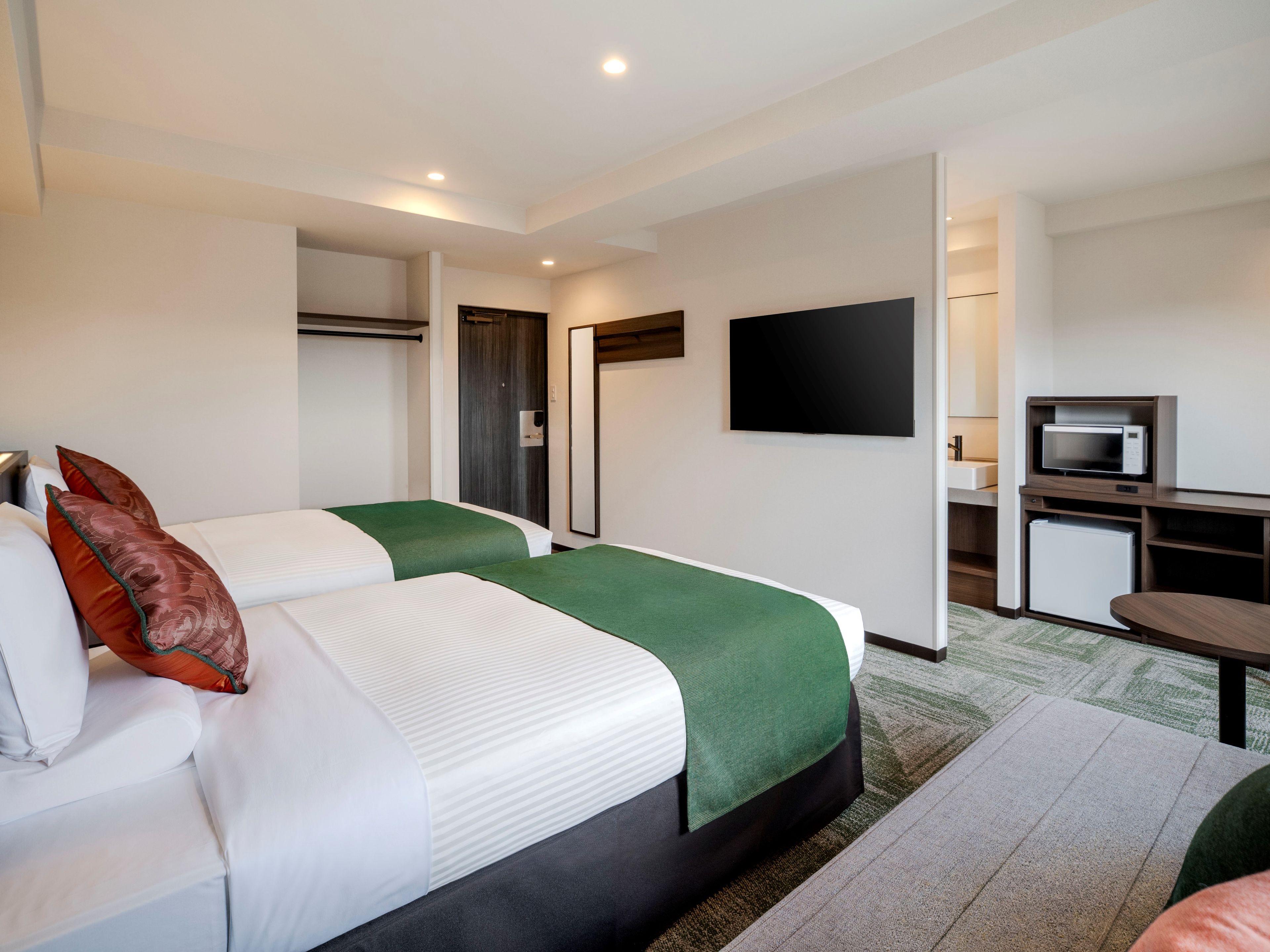 A hotel room with two beds, a flat-screen TV, a microwave, and a small kitchenette.