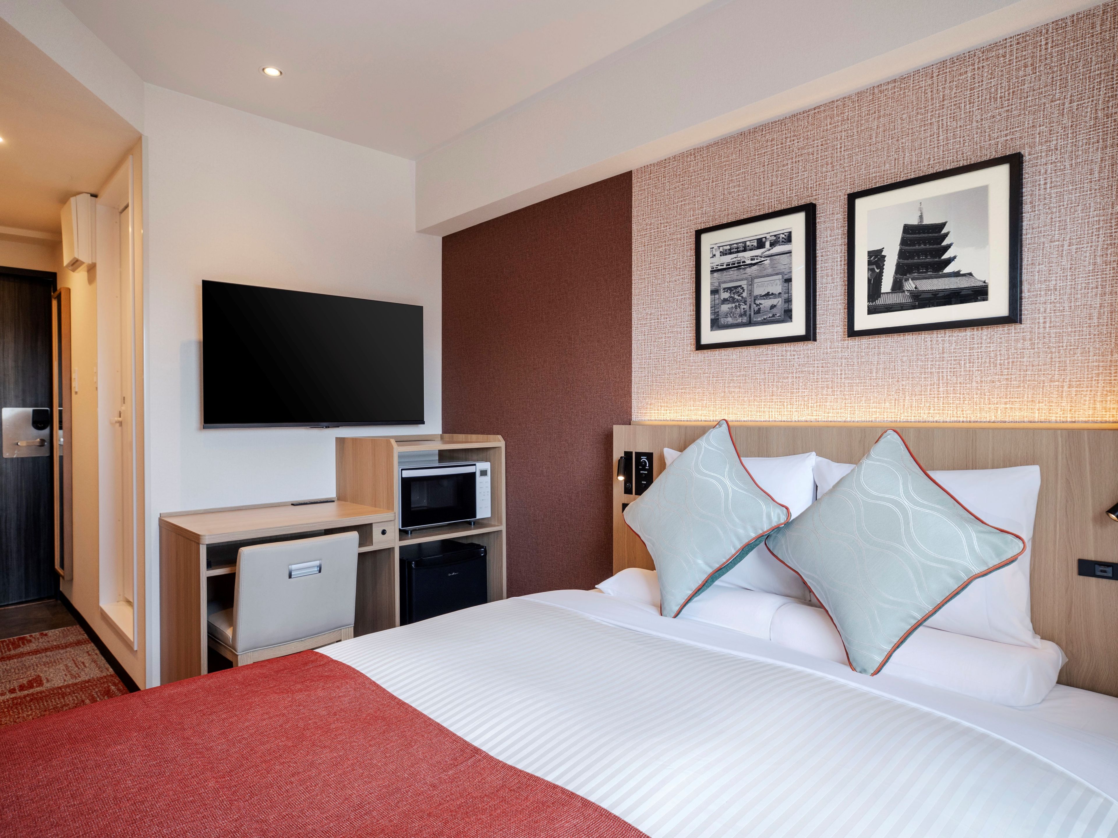 Habitación de hotel con cama, televisión, microondas, refrigerador pequeño y alfombra roja.