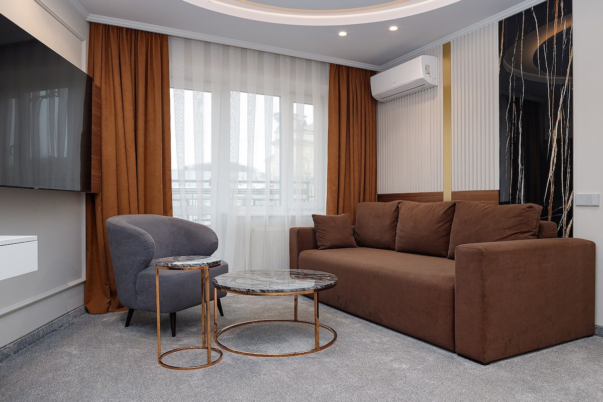 A modern living room with a brown sofa, a grey armchair, and a marble coffee table.