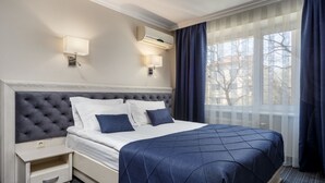 Una habitación de hotel con una cama grande, dos lámparas de noche, un equipo de aire acondicionado y una ventana con cortinas.