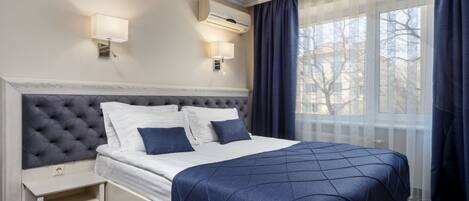 Una habitación de hotel con una cama grande, dos lámparas de noche, un equipo de aire acondicionado y una ventana con cortinas.
