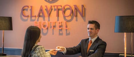 A reception desk at Clayton Hotel with a sign above displaying the hotel's name.