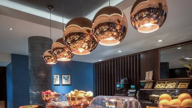 A buffet with various dishes and a modern interior with hanging spherical light fixtures. - Clayton Hotel Leopardstown (Dublin)