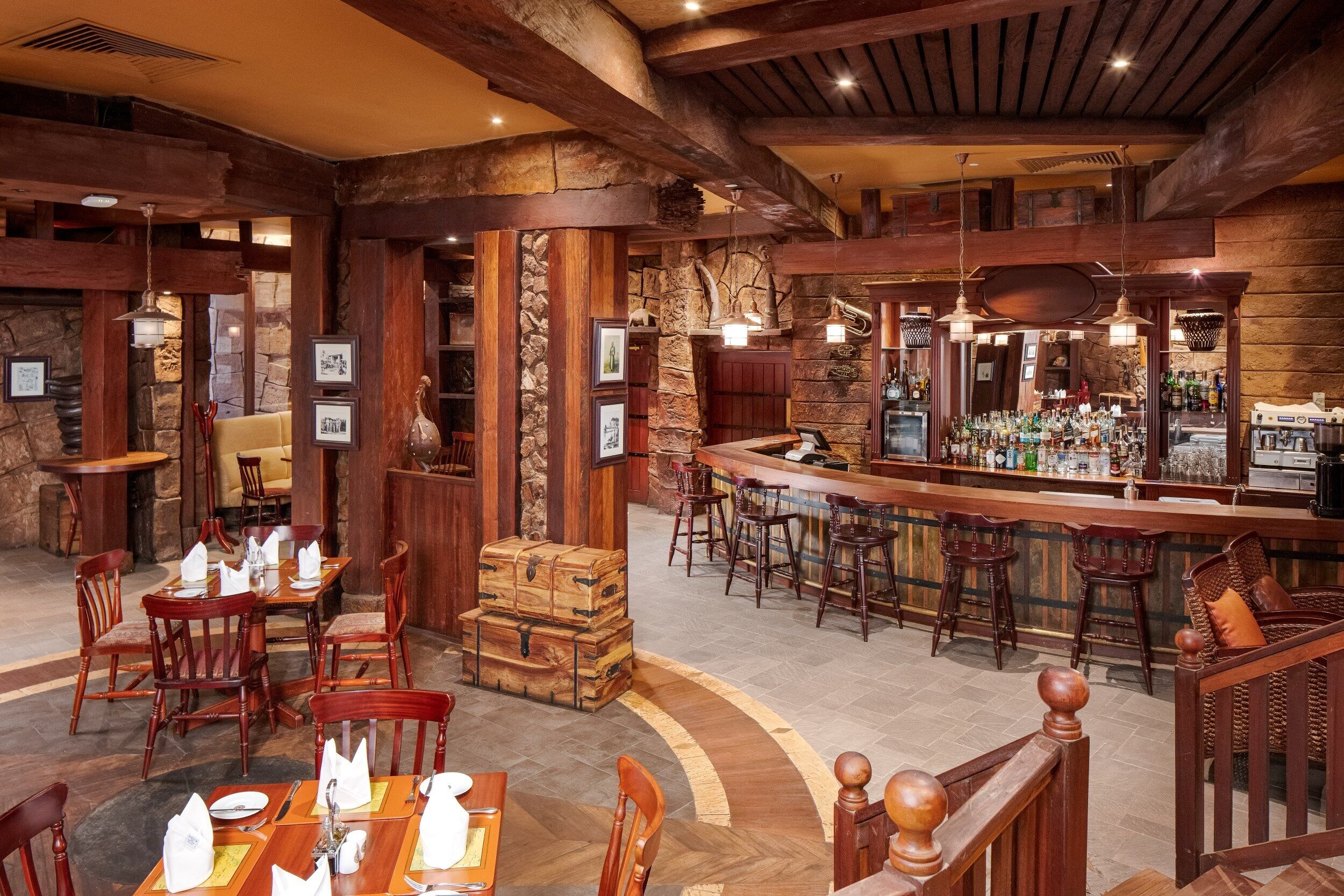 A bar area with wooden beams, stone walls, and a variety of bar stools.