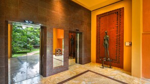 Una hall moderna con un ascensore in vetro, un'ampia porta in legno con una figura decorativa in metallo e un pavimento in marmo.