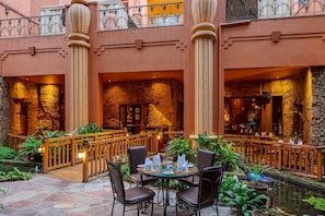 A restaurant with stone walls, wooden furniture, and a small water feature. - Kampala Serena Hotel (Kampala)