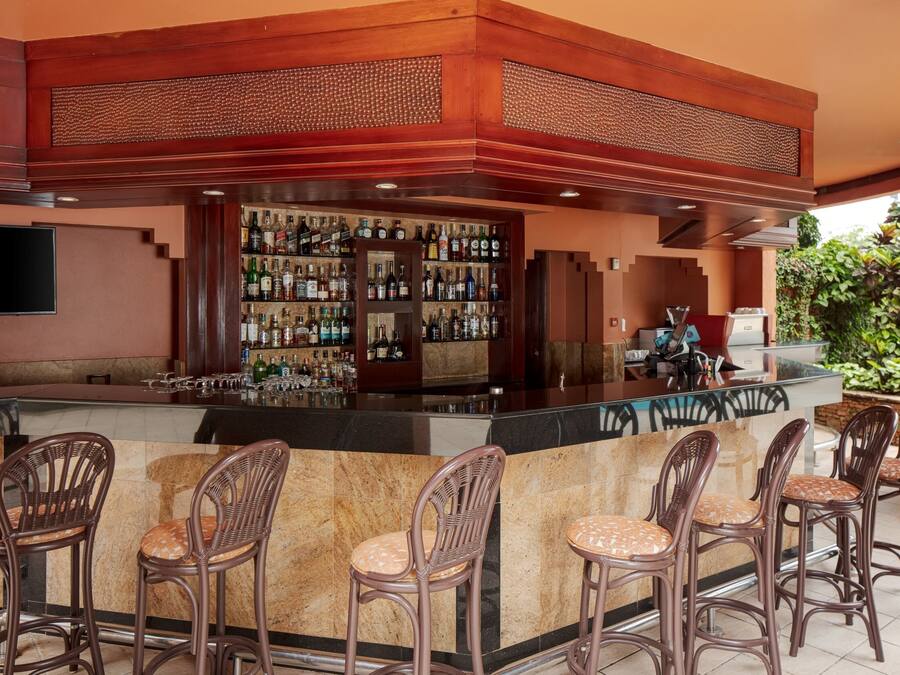 Una zona de bar con mostrador, varias botellas de licor y taburetes de mimbre.