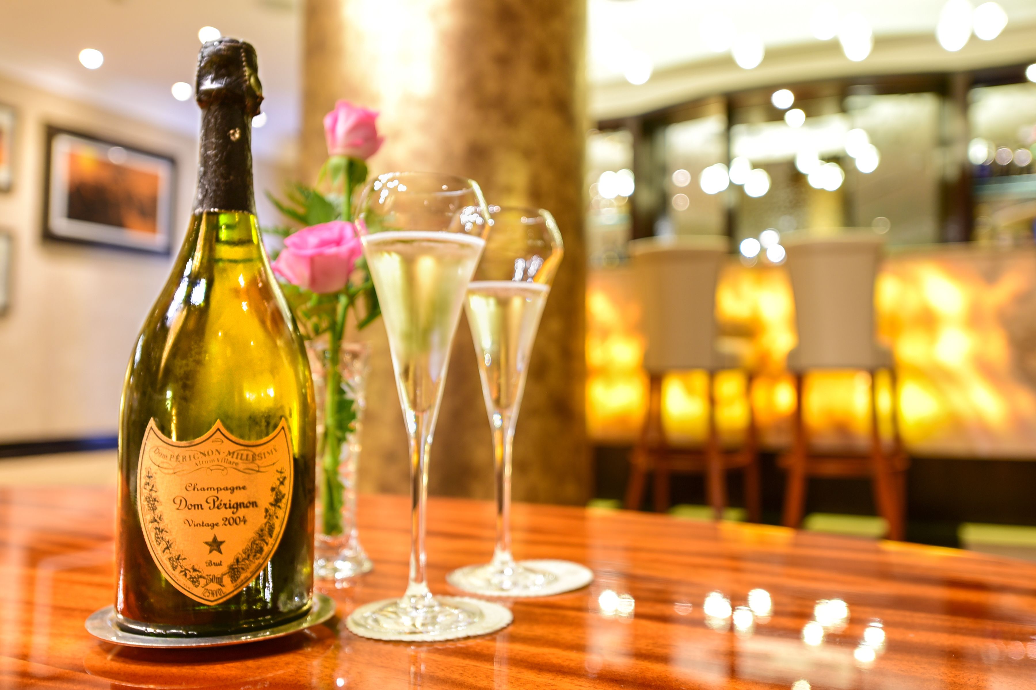 Une bouteille de champagne et deux verres sur une table en bois, dans un décor intérieur à l’éclairage chaleureux.
