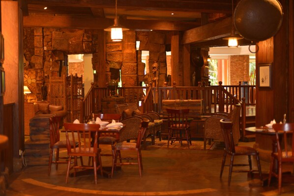 A cozy restaurant with wooden furniture, stone walls, and hanging lights. - Kampala Serena Hotel (Kampala)