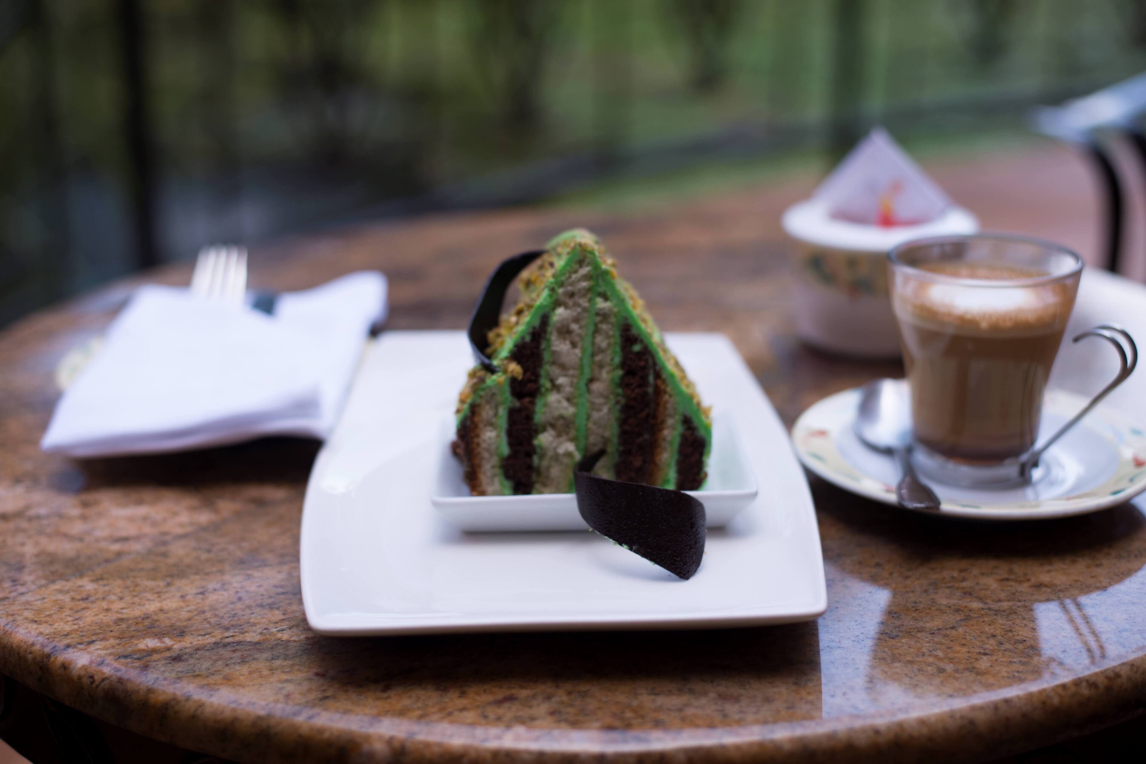 A dessert on a white plate, a cup of coffee on a saucer, and a fork on a napkin on a round table.