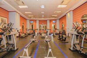 A gym with multiple exercise machines, a clock on the wall, and a TV screen. - Kampala Serena Hotel (Kampala)