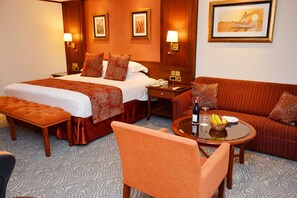 A hotel room with a large bed, a sofa, a round table with a bottle and fruit, and artwork on the walls. - Kampala Serena Hotel (Kampala)