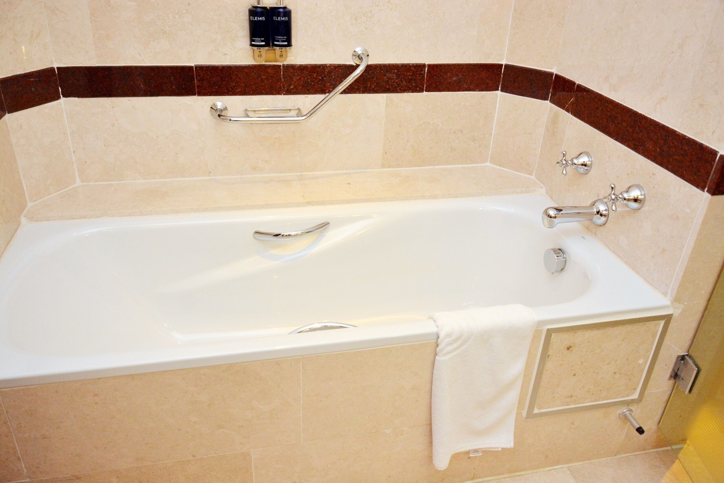 A modern bathroom with a bathtub, grab bars, and a towel rack.