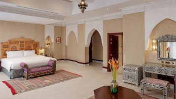 Amplia habitación de hotel con una cama grande, una zona de estar con sofá y una mesa de centro, y un espejo decorativo.