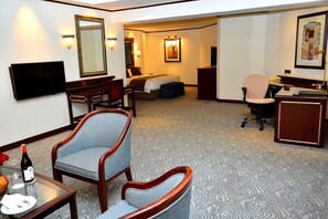 A hotel room with a bed, a desk, a chair, a television, and a desk lamp. - Kampala Serena Hotel (Kampala)