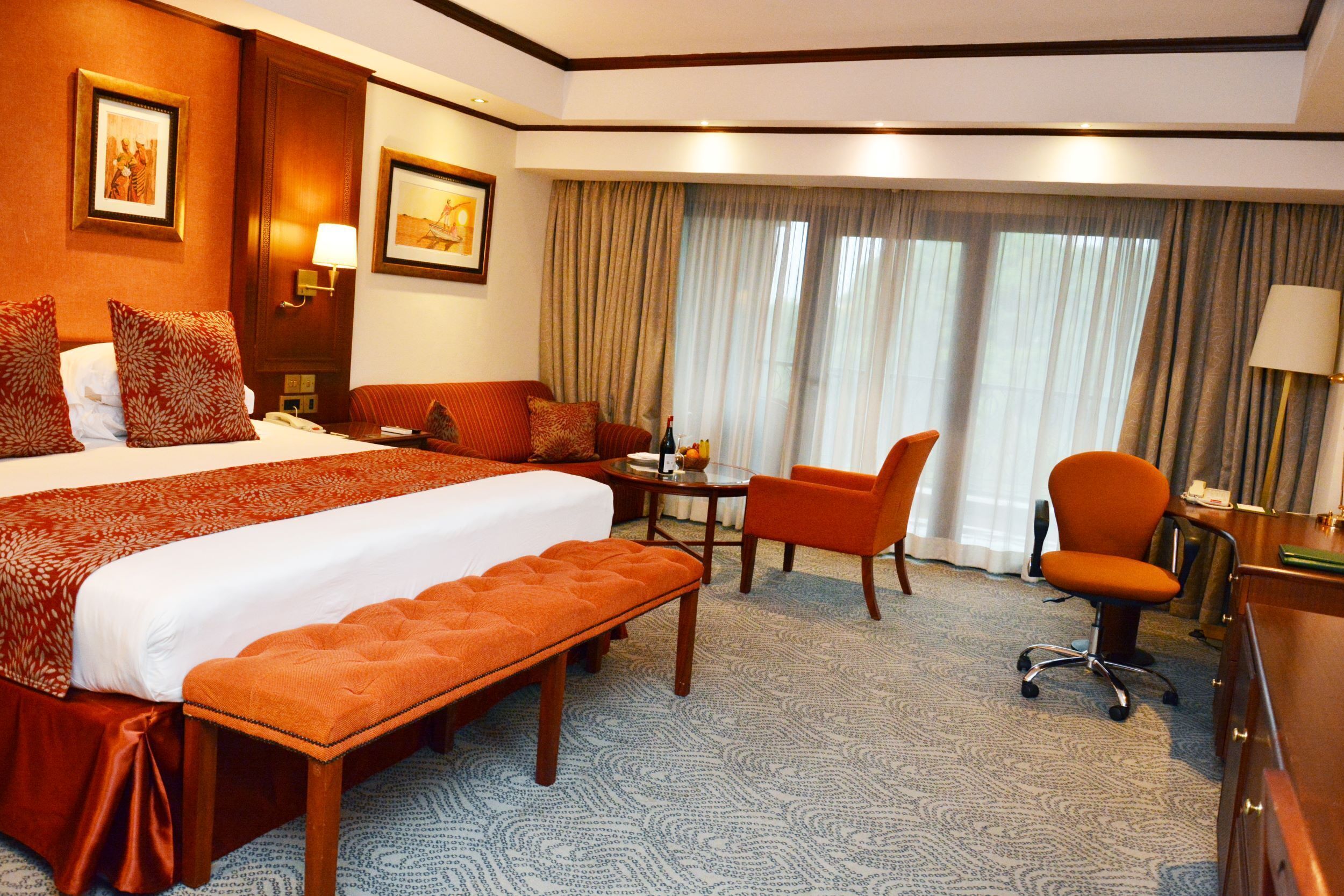 Une chambre d’hôtel avec un grand lit, un bureau, deux chaises, un banc et une vue sur l’extérieur par la fenêtre.
