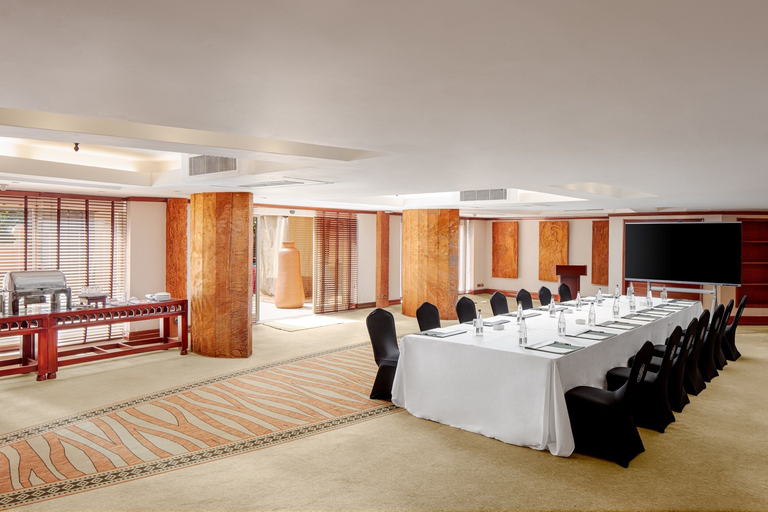 A conference room with a long table, chairs, a projector screen, and a large window with blinds.