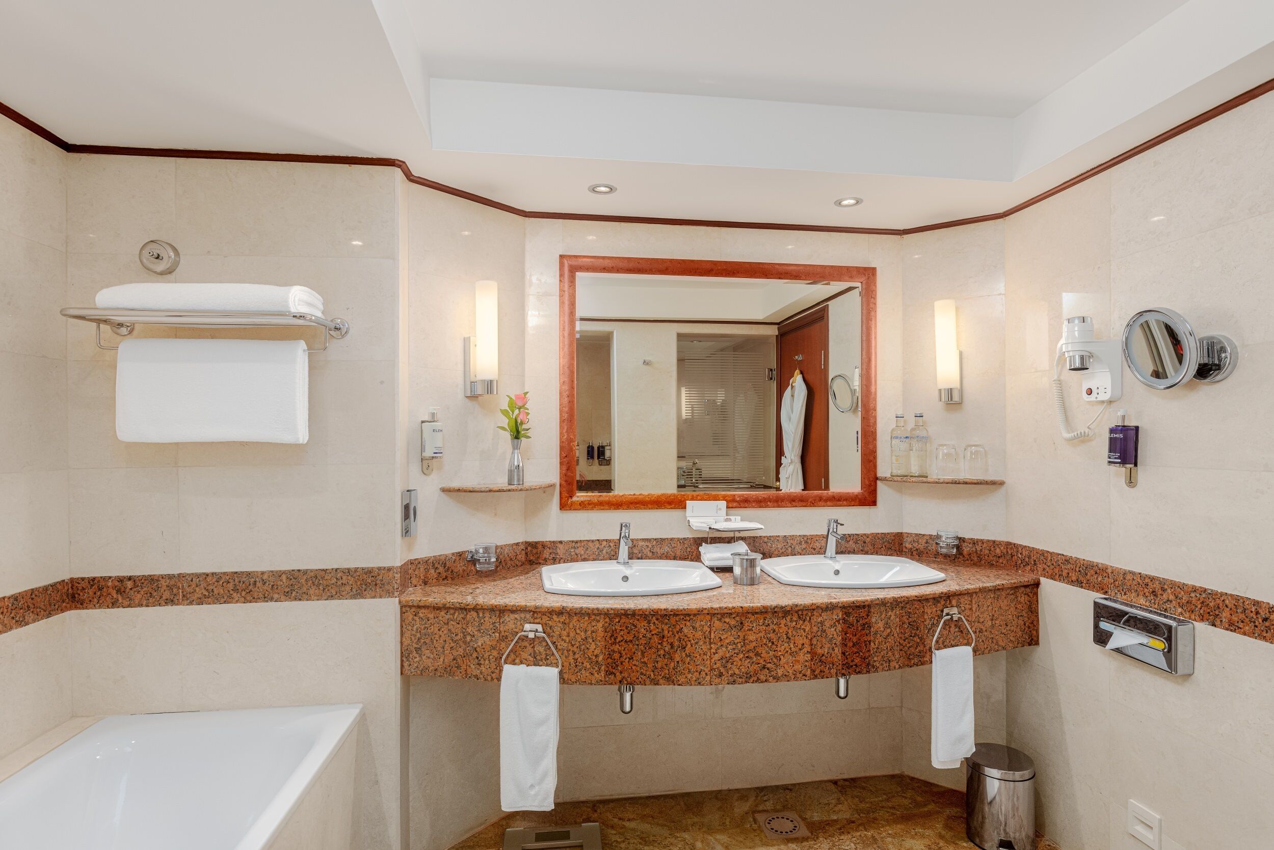 A hotel bathroom with two sinks, a bathtub, a large mirror, and a towel rack.