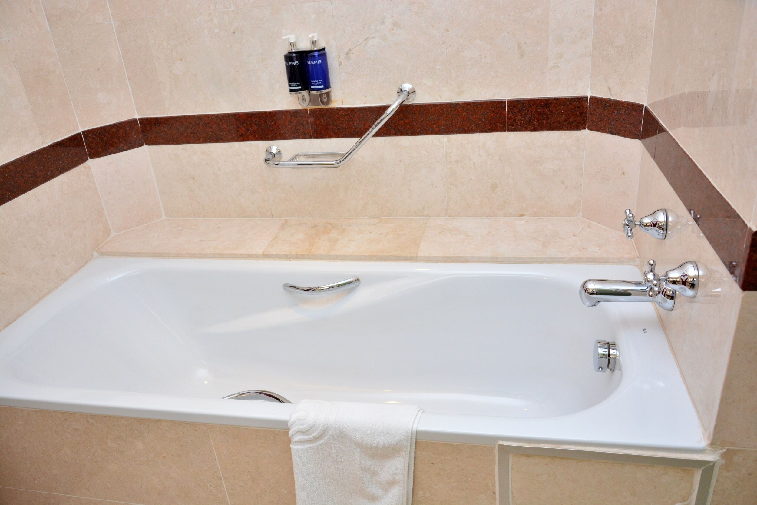 A bathroom with a bathtub, a handrail, and two bottles of toiletries on the wall.