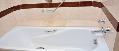 A bathroom with a bathtub, a handrail, and two bottles of toiletries on the wall.