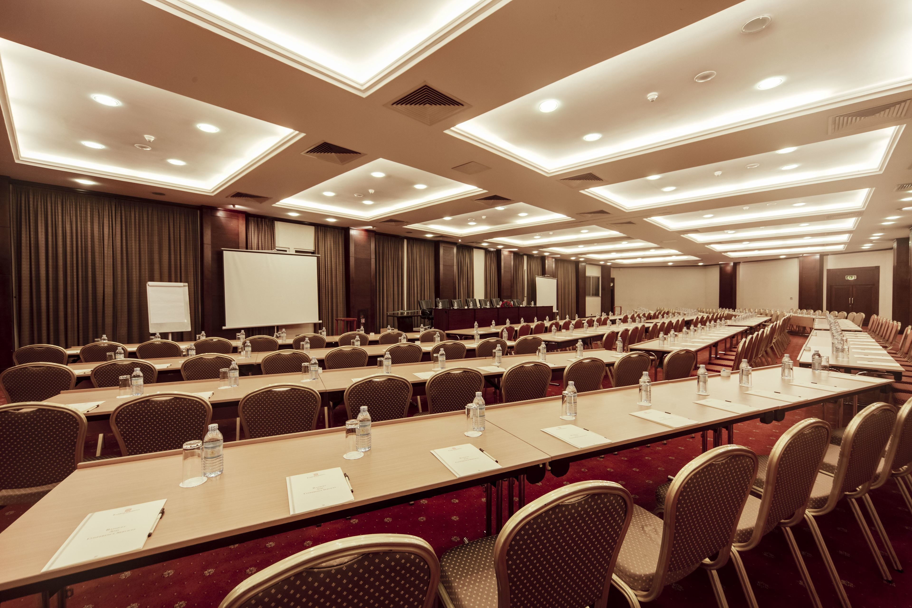 Una sala de conferències amb taules llargues, cadires i una pissarra.
