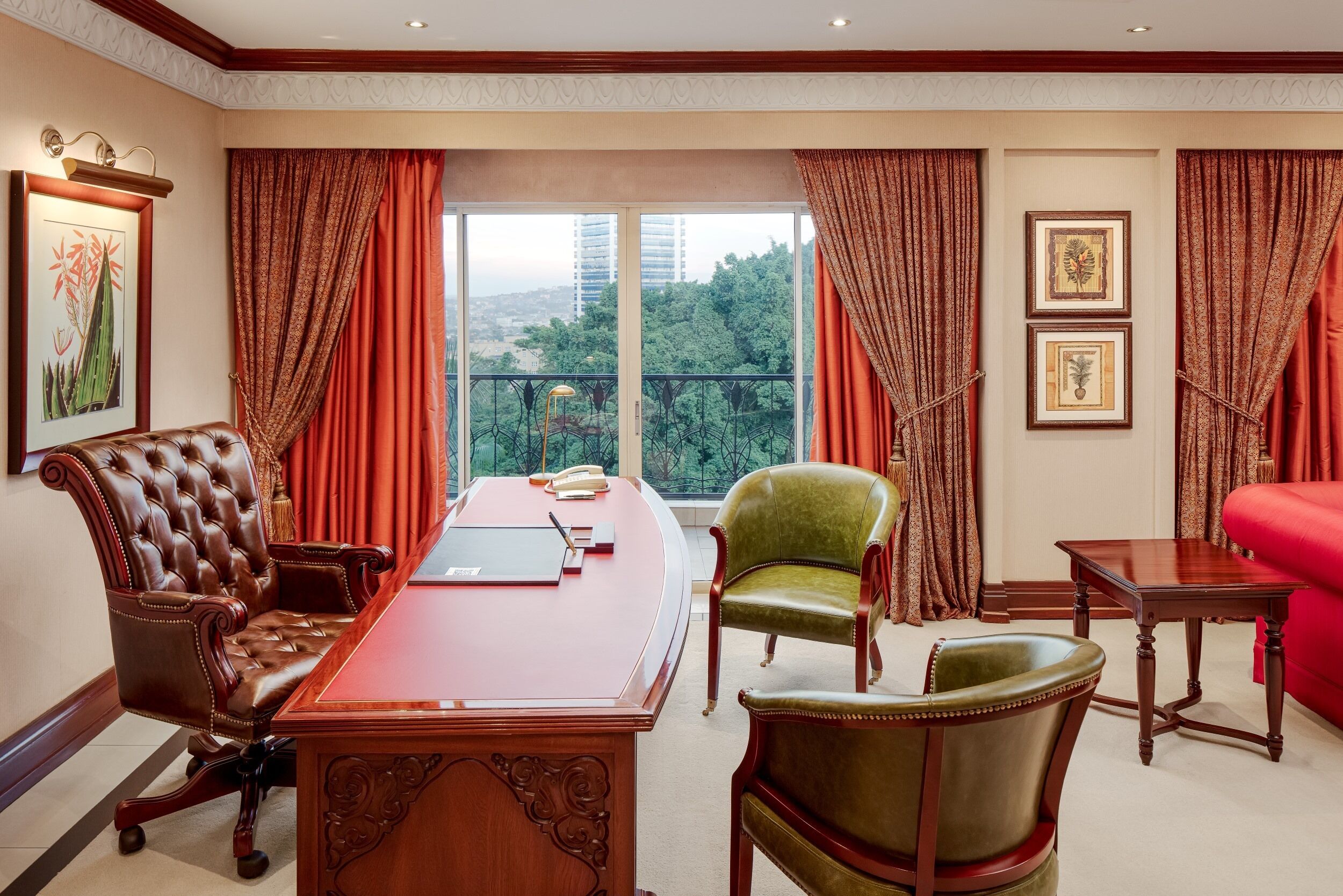 A conference room with a large wooden table, leather chairs, a red sofa, and a view of greenery through large windows.