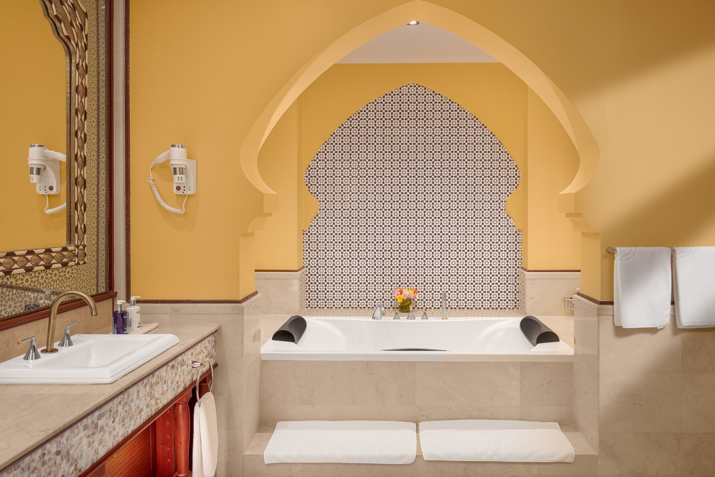 A bathroom with two sinks, a large mirror, a towel rack, and a patterned wall.