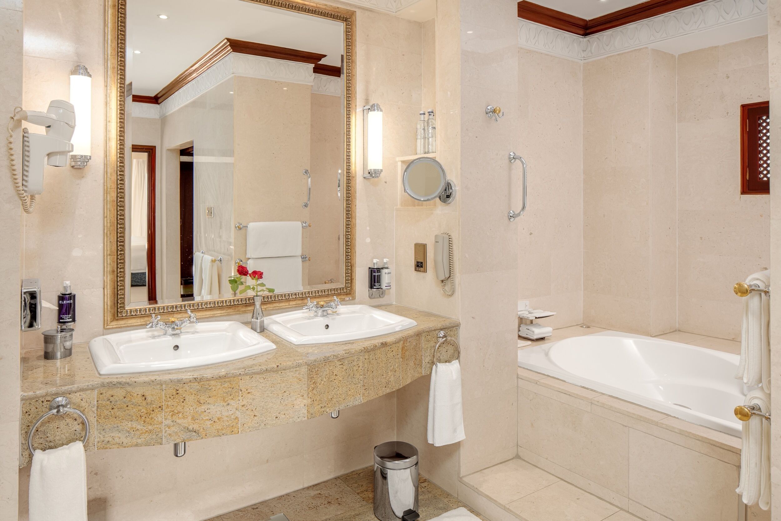 A hotel bathroom with two sinks, a large mirror, a bathtub, and a shower.