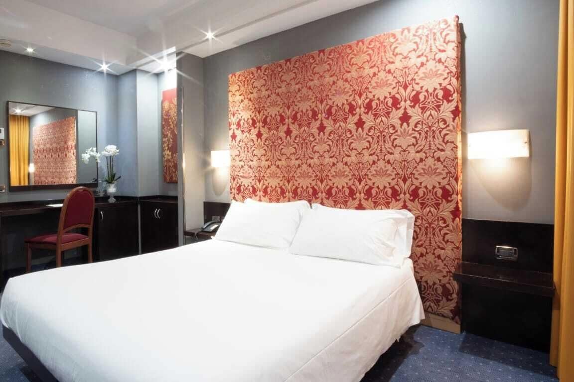 Een hotelkamer met een groot bed, een bureau met stoel, een spiegel en een decoratieve wand.