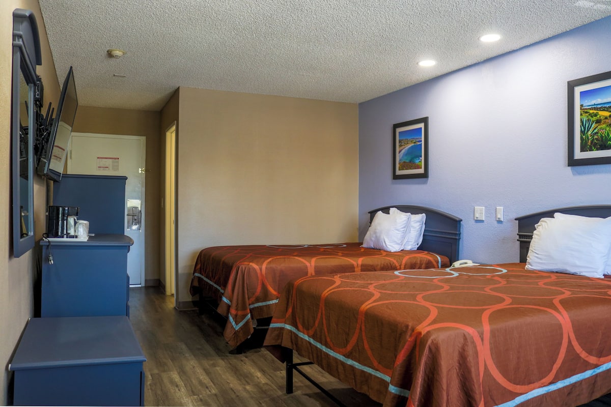 A hotel room with two beds, a desk, a coffee machine, and a refrigerator.