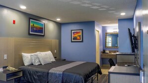 A hotel room with a bed, bedside table, desk, and a mirror. - Orange Tustin Inn (Orange)