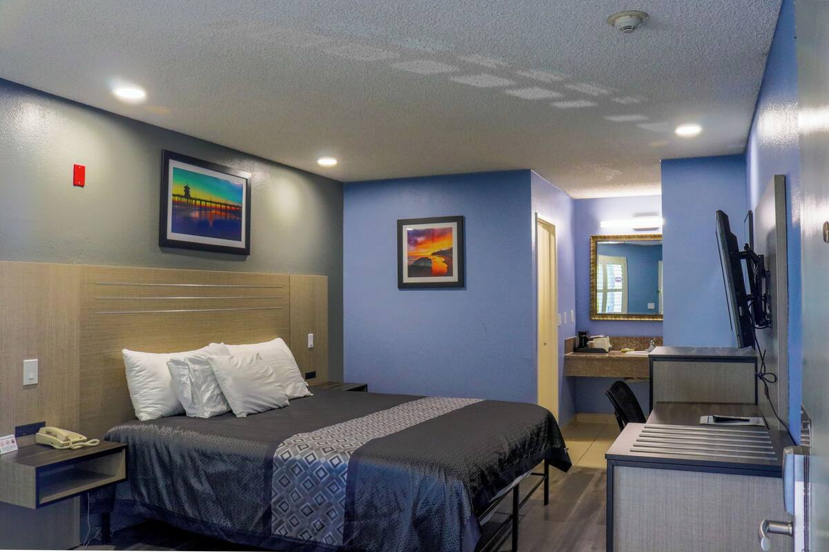A hotel room with a bed, bedside table, desk, and a mirror.
