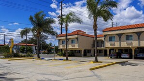 A parking lot with a building that has multiple garages and a covered area. - Orange Tustin Inn (Orange)