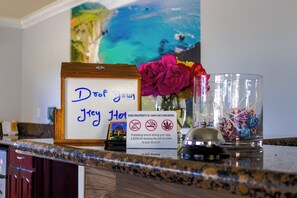 A hotel reception desk with a framed sign, a vase of flowers, and a glass container with candies. - Orange Tustin Inn (Orange)