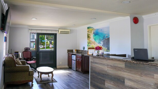 A hotel lobby with a reception desk, a sofa, a coffee table, a painting, and a laptop on the counter. - Orange Tustin Inn (Orange)