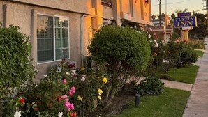 A building with a stucco exterior, multiple balconies, and a well-maintained garden with various flowers. - Orange Tustin Inn (Orange)