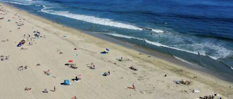 A wide beach with people and umbrellas, a clear sky, and the ocean.