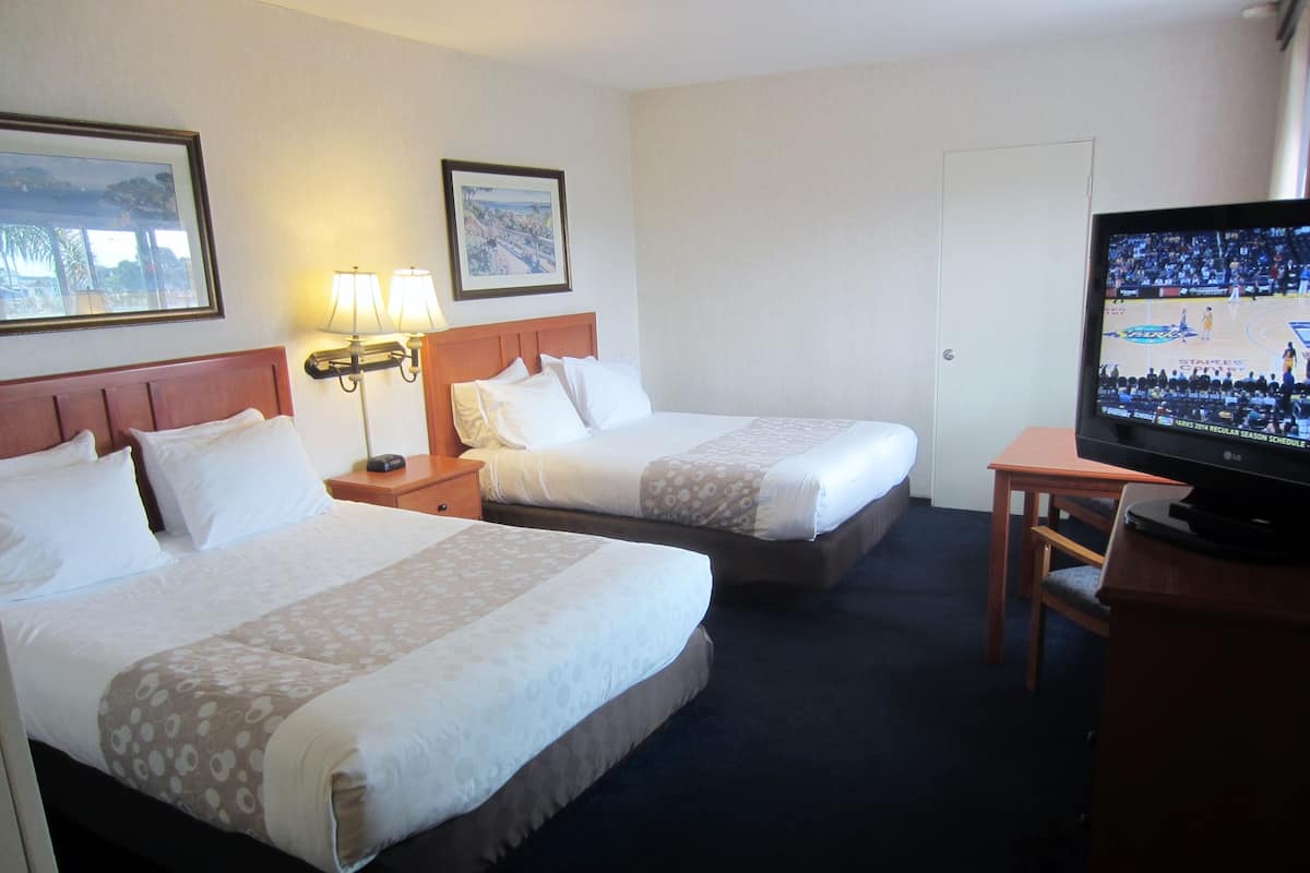 A hotel room with two beds, a television, and a desk.