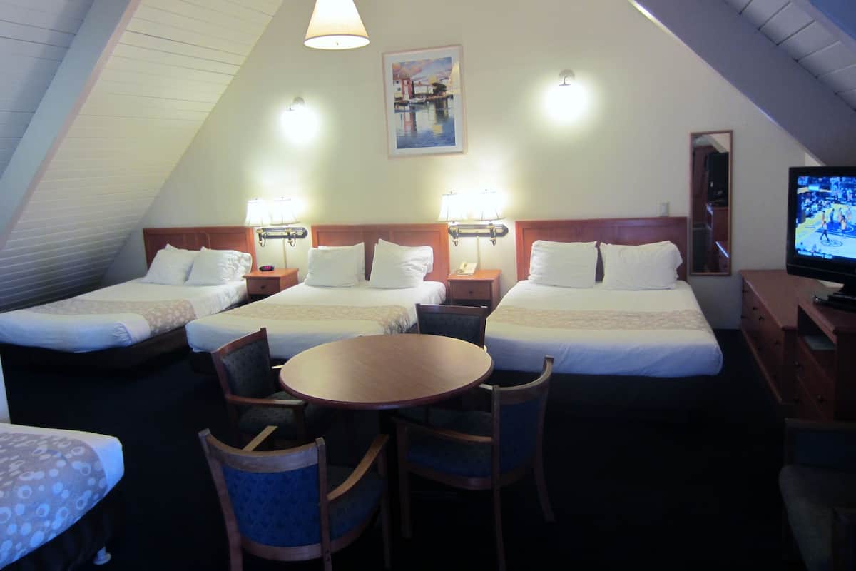 A hotel room with two beds, a dining table, chairs, a TV, and a painting on the wall.