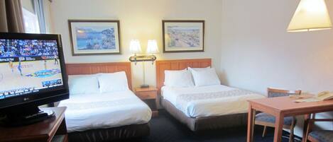 Quarto de hotel com duas camas, uma escrivaninha, uma televisão e duas luminárias fixadas na parede.