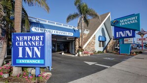 The entrance to Newport Channel Inn with clear signage, a stone facade, and a palm tree in the background. - Newport Channel Inn - Near Huntington State Beach (Newport Beach)