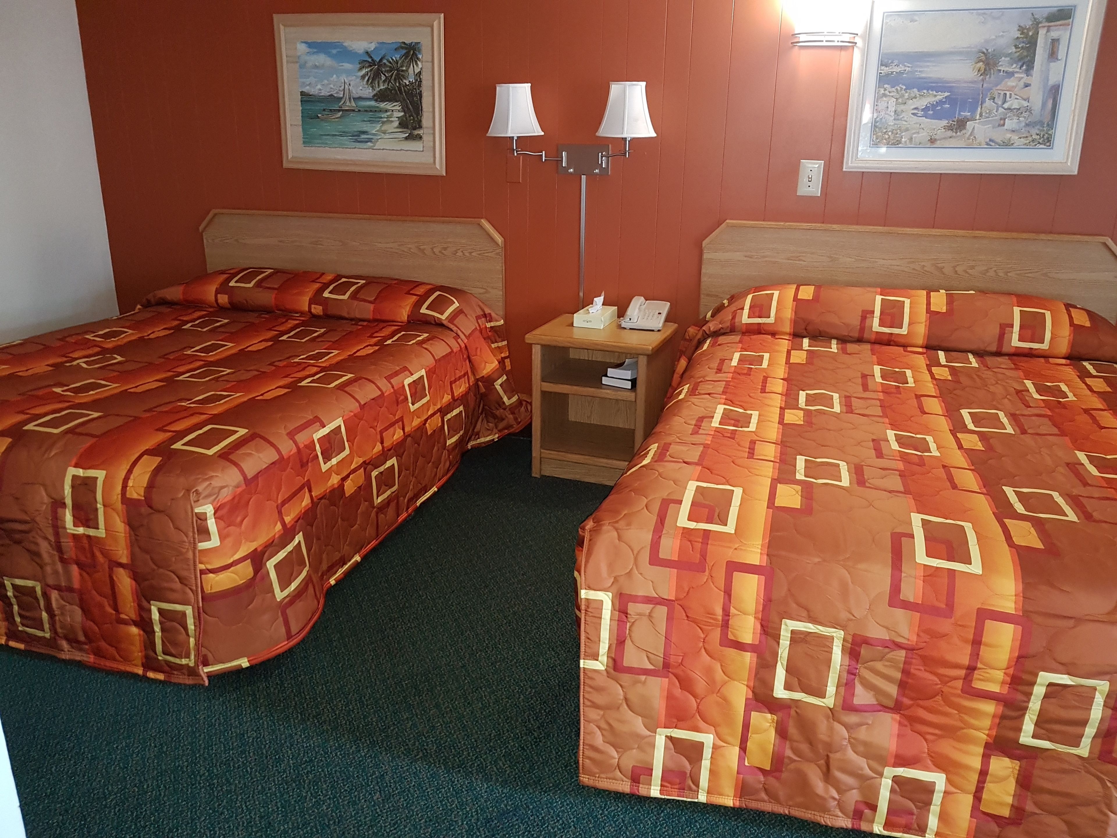 Una habitación de hotel con dos camas, una mesita de noche con lámpara y dos cuadros en la pared.