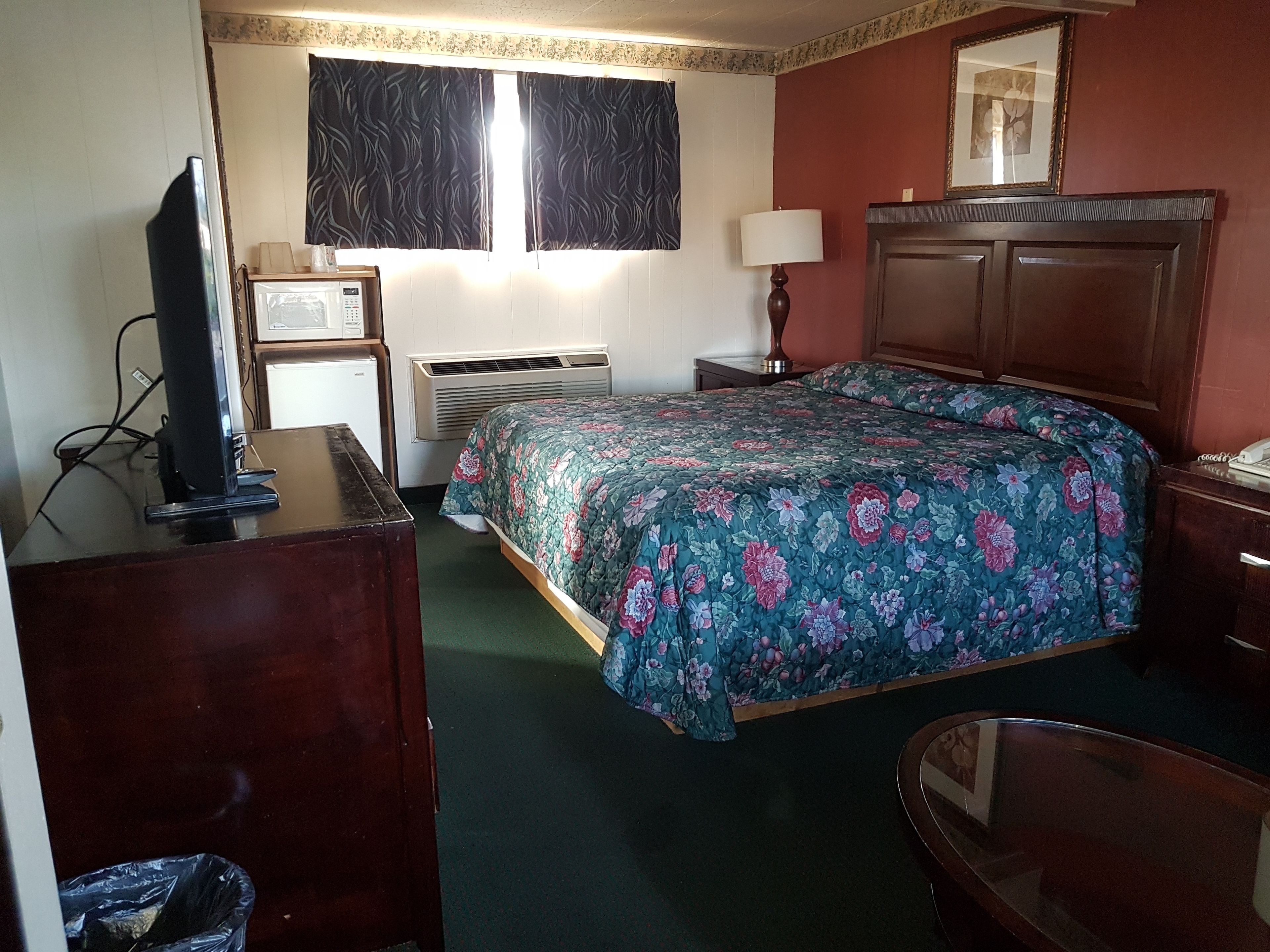 A hotel room with a bed, a desk, a television, a lamp, and a picture on the wall.