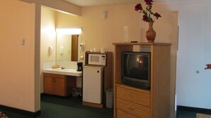 Quarto de hotel compacto com cozinha compacta, micro-ondas, geladeira, televisão e um vaso com flores em uma cômoda.