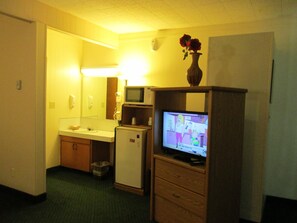 A hotel room with a kitchenette, a small refrigerator, a microwave, a television, and a vase with flowers on the dresser. - Town House Motel Inc (Longview)