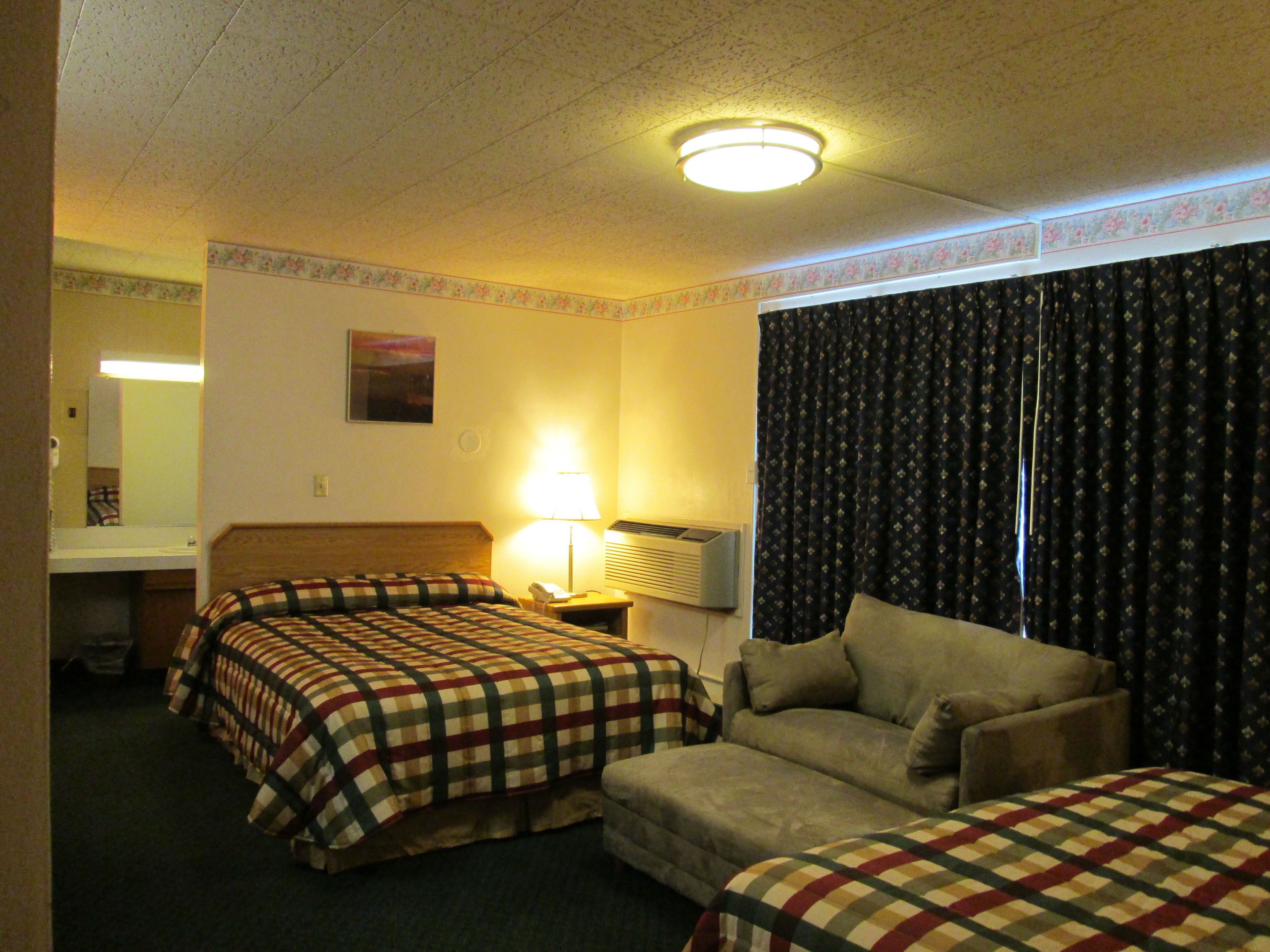 Habitación de hotel con dos camas, un sofá, una lámpara y un ventanal con cortinas.